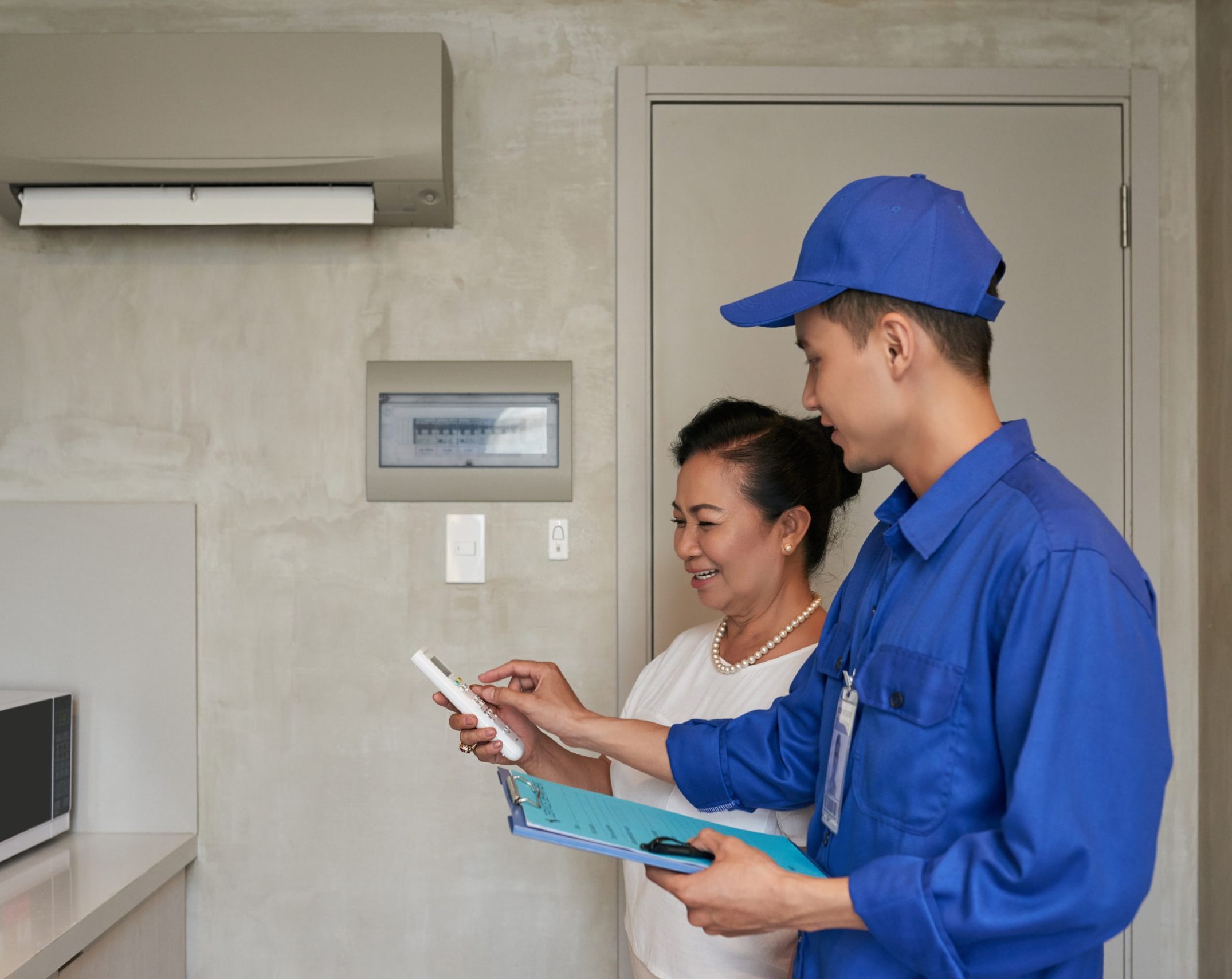 Technician explaining senior Vietnamese woman how to use air conditioner